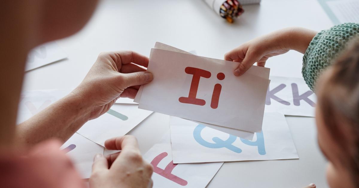 A person holds up the printed letter "I" to show a child. 