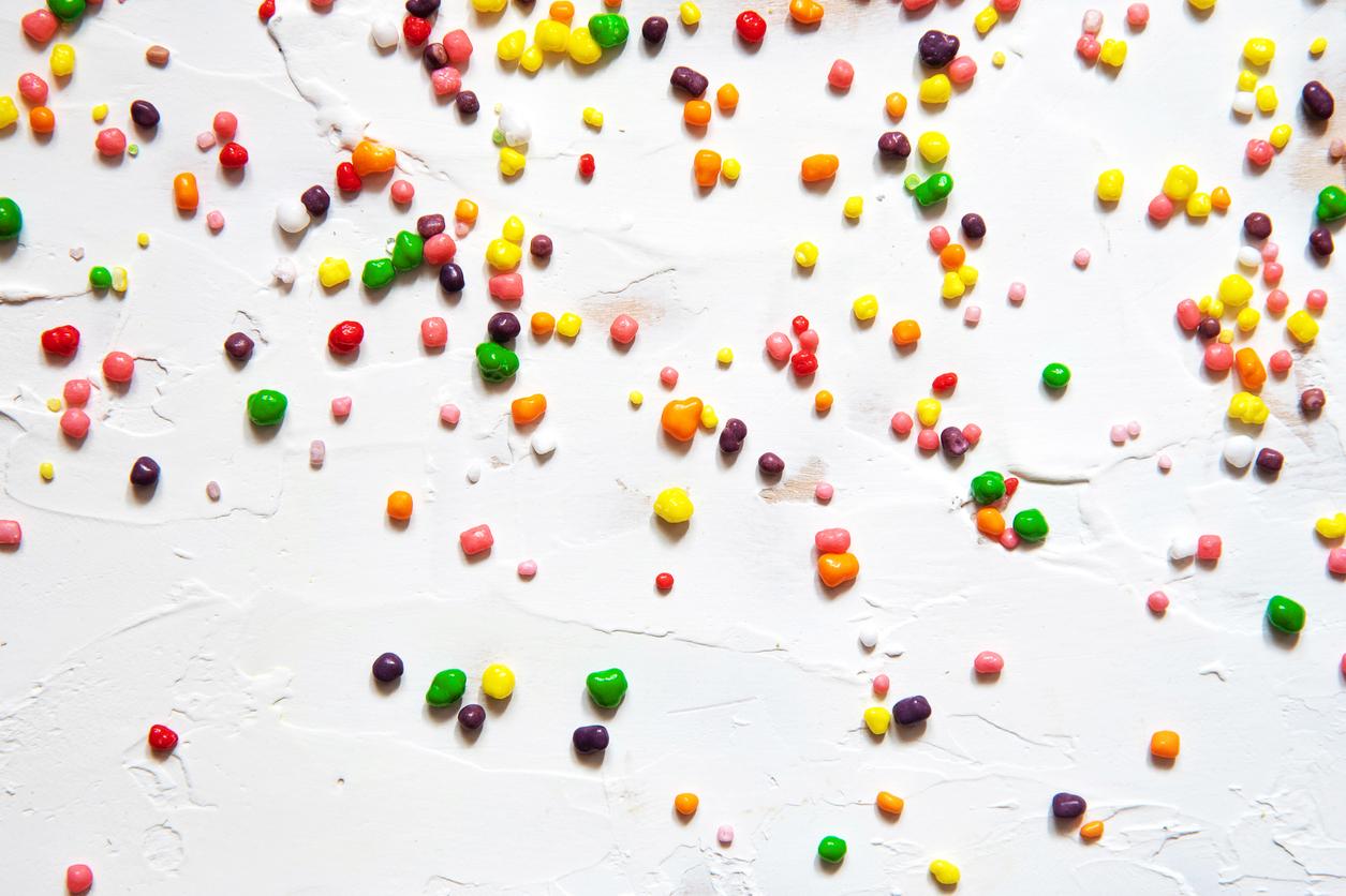 Rainbow colored candy of various sizes spilled across a white background