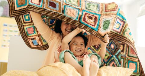 An mother and her child playing with a crochet blanket.