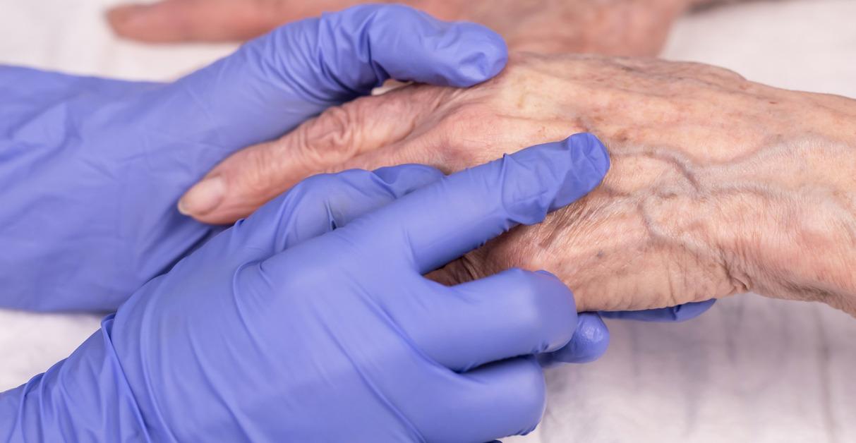 A person wearing blue gloves points at the veins on an older person's hand.