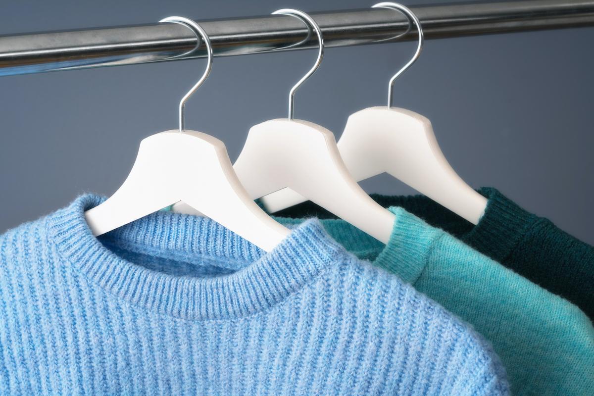 Three sweaters in shades of blue on hangers