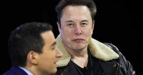Elon Musk wears a jacket with a fur color with a man's side profile in the foreground.