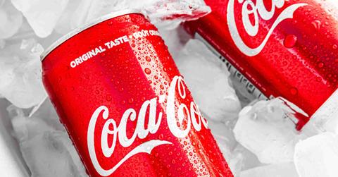 Two cans of Coca-Cola are pictured nestled into a container with ice.