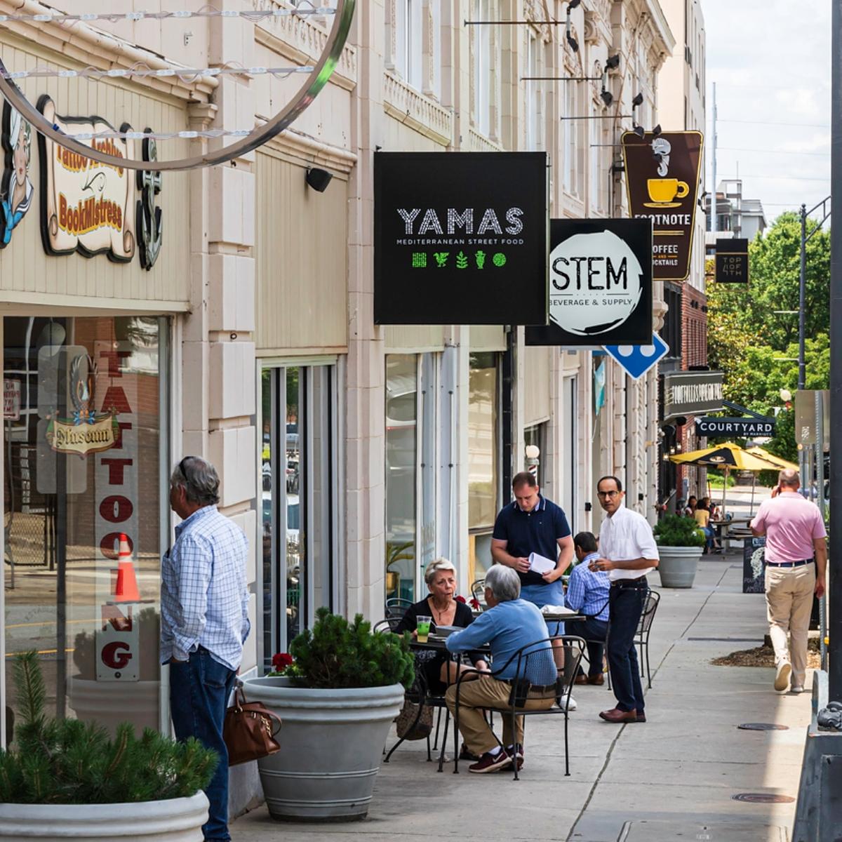 Photo of Winston-Salem, N.C., residents and visitors eating at outdoor tables along a city sidewalk 