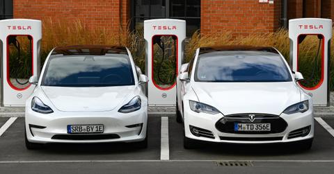 A front view of two white Tesla cars charging at a Tesla charging station in front of a brick building.