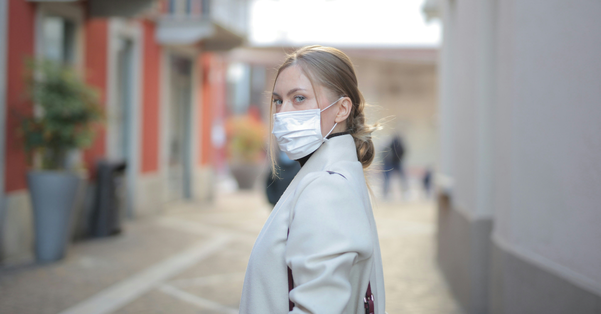 A masked woman stands on a semi-empty street