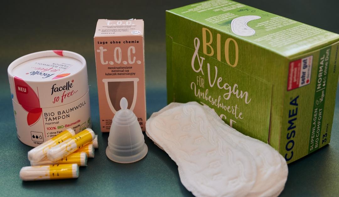 Sustainable feminine hygiene articles from different manufacturers, including panty liners, a menstrual cup, and tampons are pictured on a table