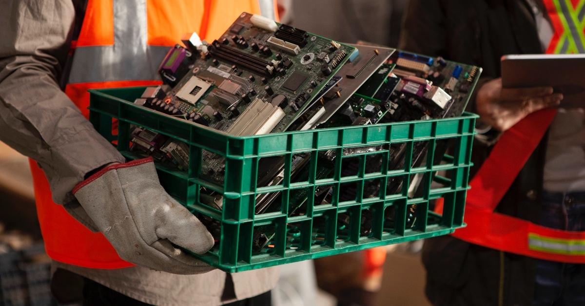 Person carrying circuit boards in green plastic bins from factories to be recycled. 