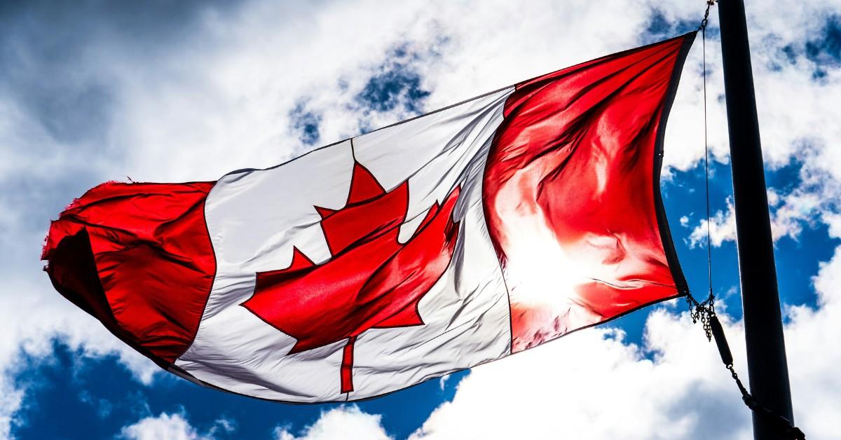 A Canadian flag blows in the wind against a bright blue sky