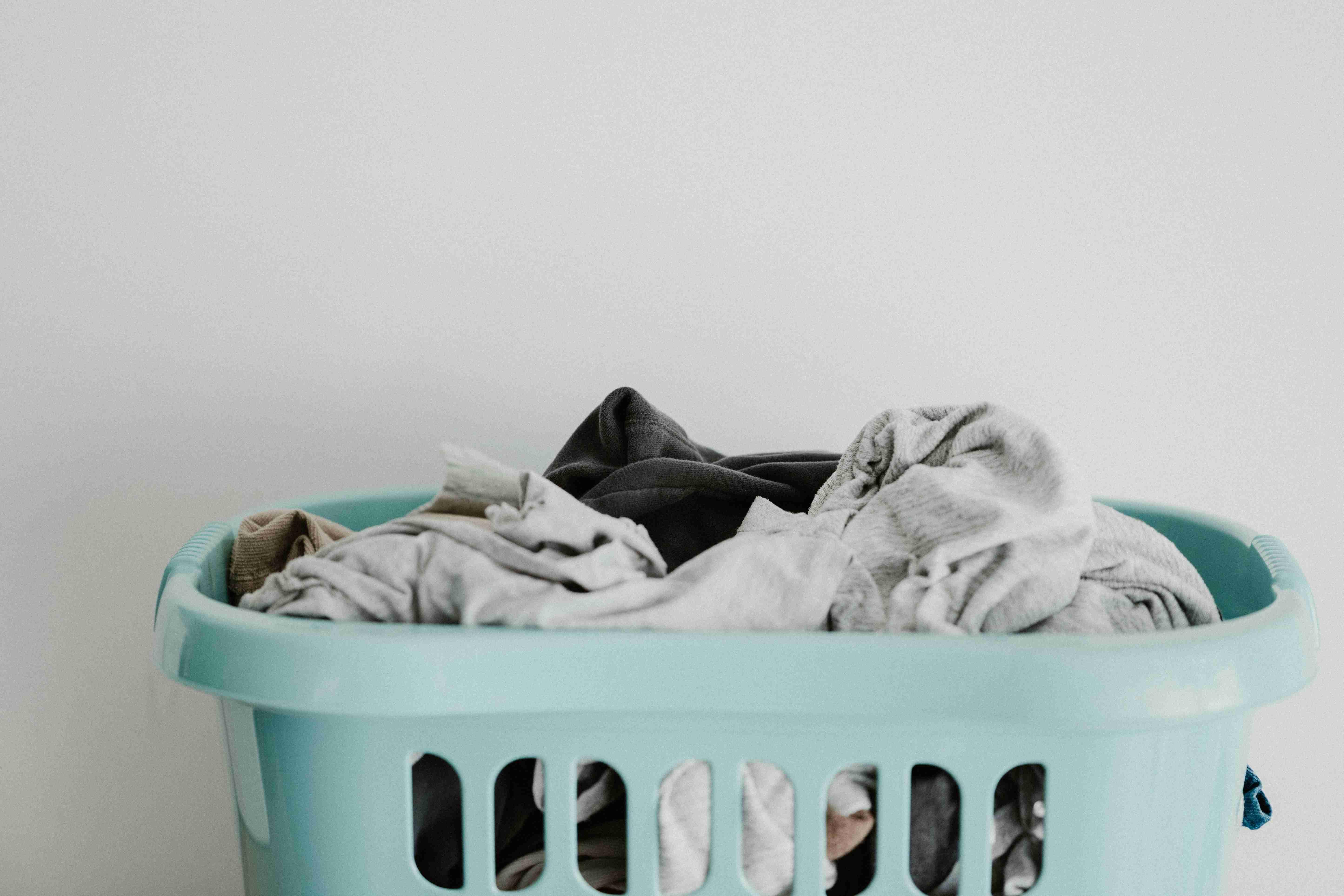 A green laundry basket with holes is pictured with various laundry inside it.