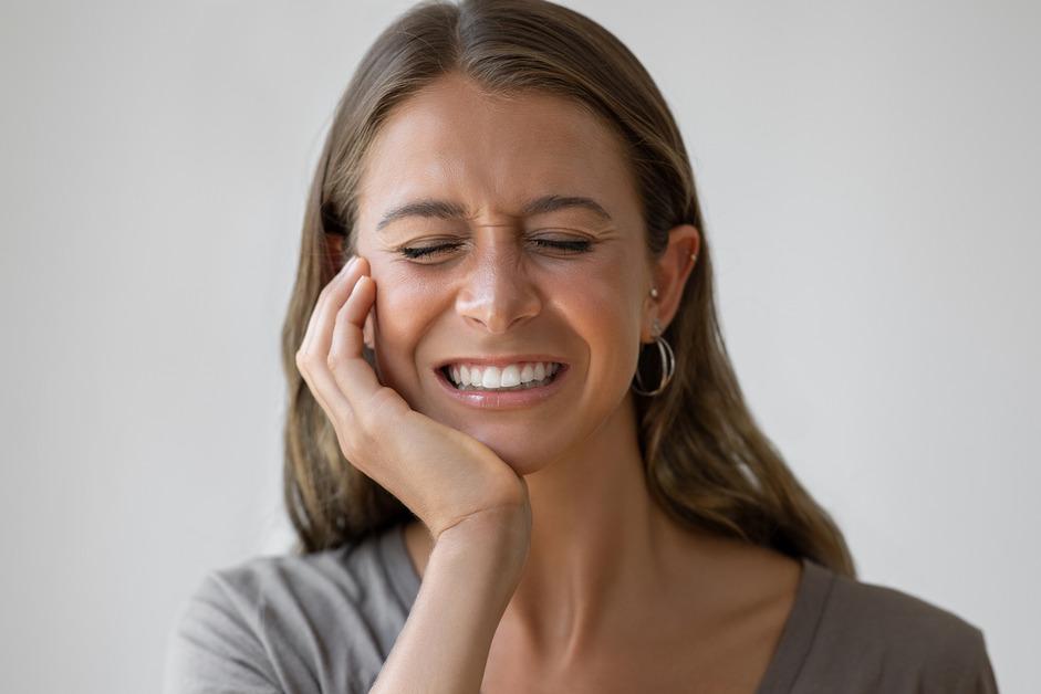 A woman squeezes her eyes shut while holding the side of her face in pain.