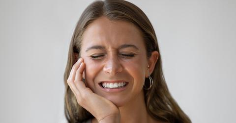 A woman squeezes her eyes shut while holding the side of her face in pain.