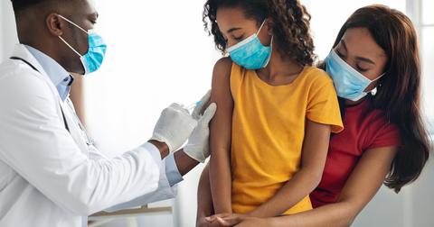 A daughter sits on her mothers lap while receiving a vaccine from a male doctor.