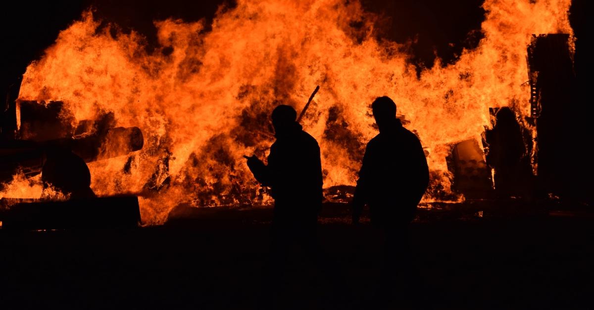 Two fighterfighters in front of a large wildfire.