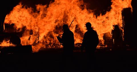 Two fighterfighters in front of a large wildfire.