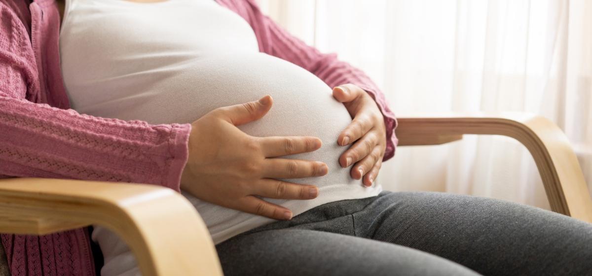 Pregnant woman in white shirt and pink sweater touching her baby bump