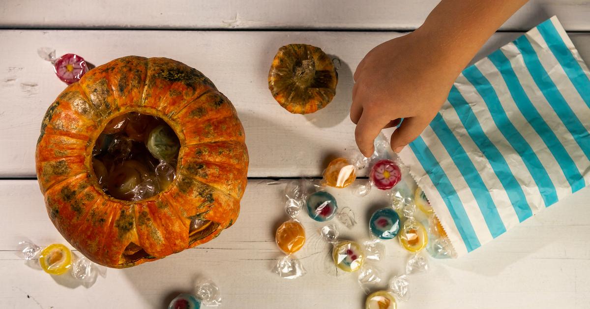 Kid's hand reaches for candy next to a pumpkin