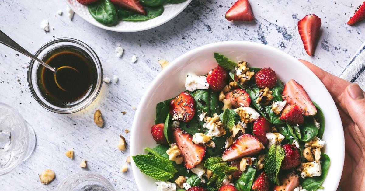 A bowl of salad sits next to a jar of salad dressing