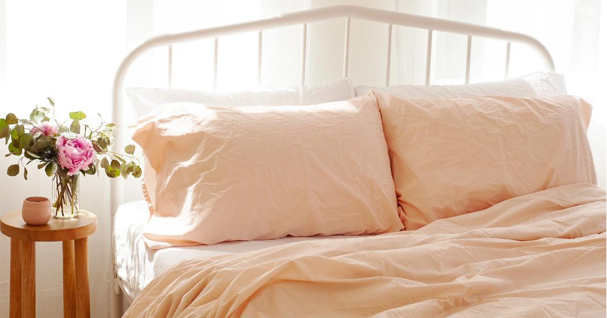 a bed made in peach sheets and a night table with flowers and a candle