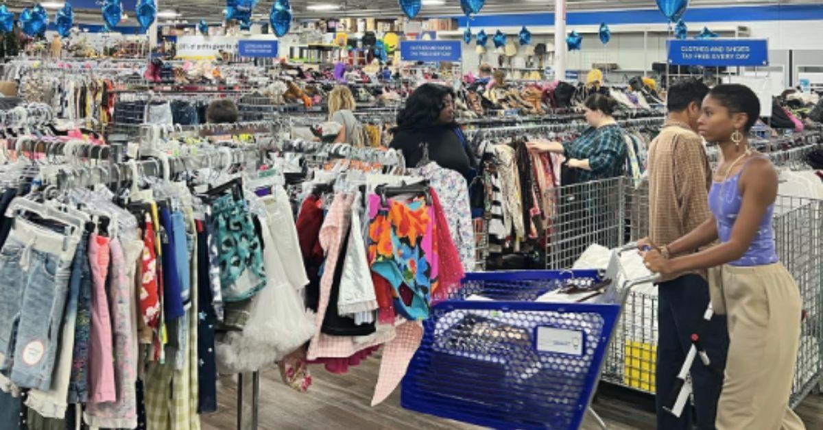 Clothing racks in a store and shoppers pushing carts.