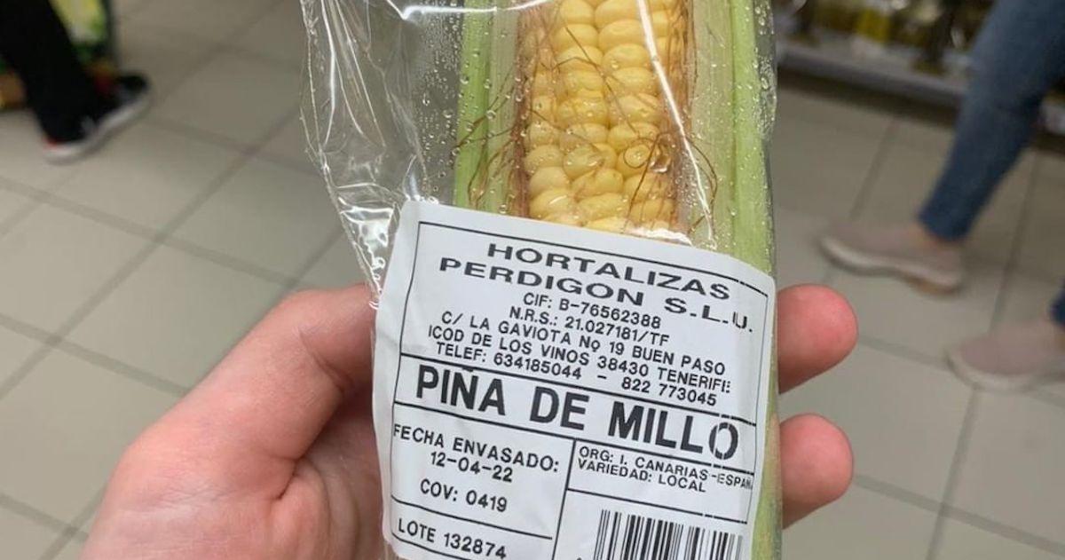 Hand holds an ear of corn in plastic packaging with a label