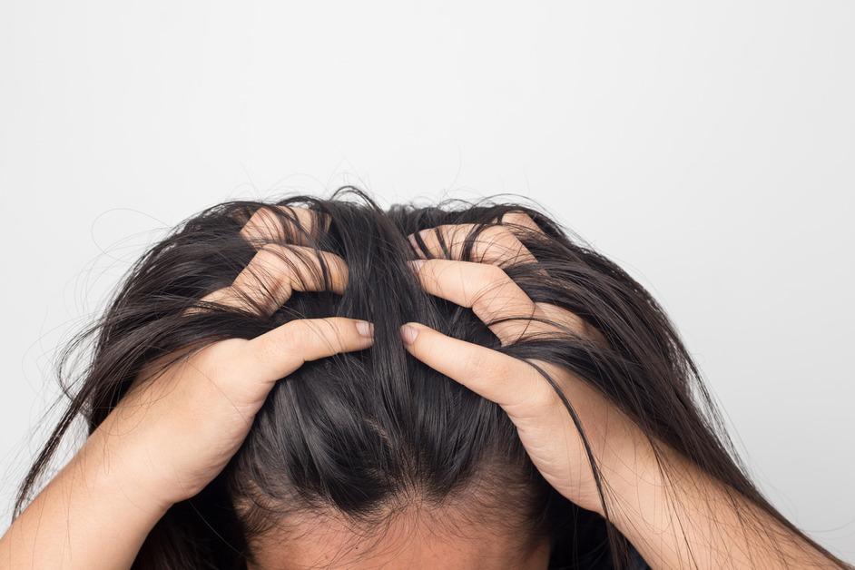 A person with dark hair grips the top of their head in pain.