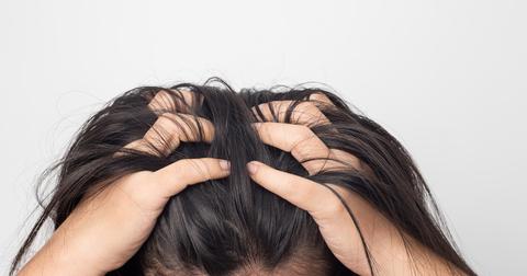 A person with dark hair grips the top of their head in pain.