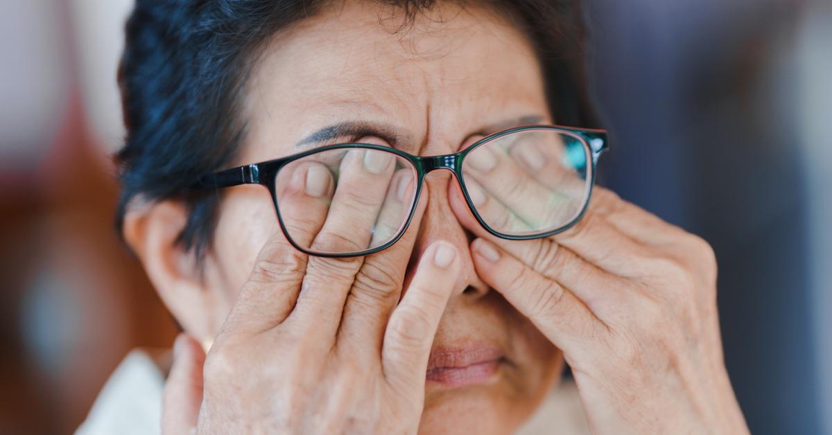 Woman rubs her red eyes beneath glasses. 