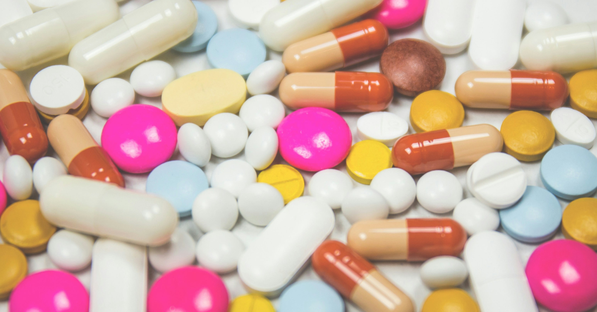 A collection of pills is laid out in a pile, featuring pink, white, blue,  yellow, and two-toned options