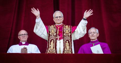 Pope Leo XIV stands on a balcony smiling at the people gathered below