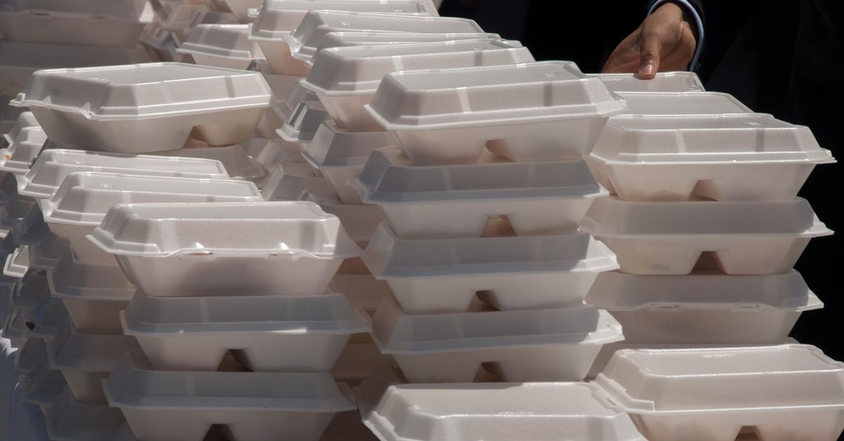 Stack of white takeout boxes atop a table, a hand in the right corner reaches to take one.