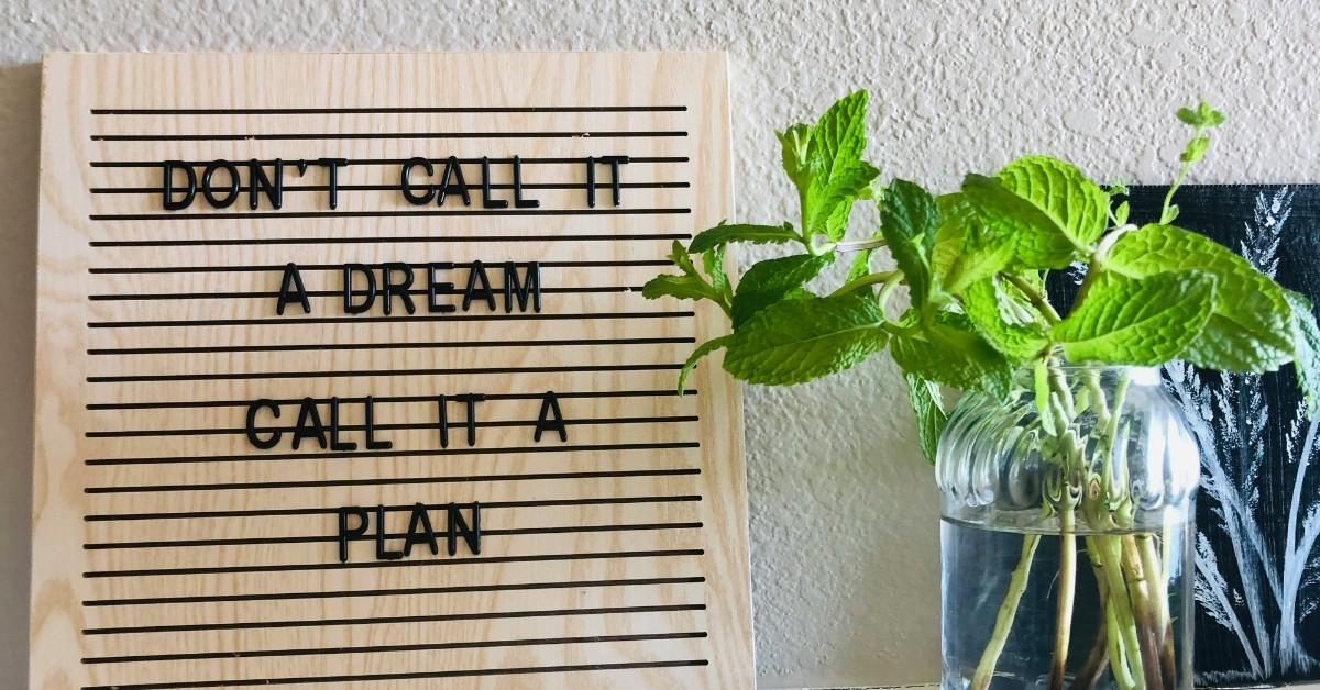 A sign reads "don't call it a dream, call it a plan" next to a plant