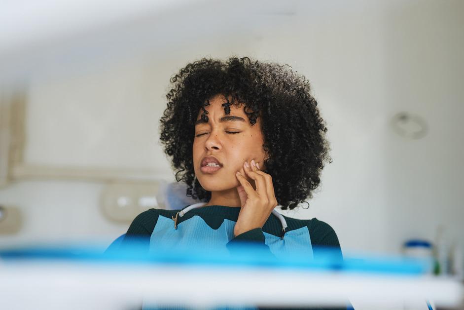 A woman at the dentist holds the side of her mouth in pain. 