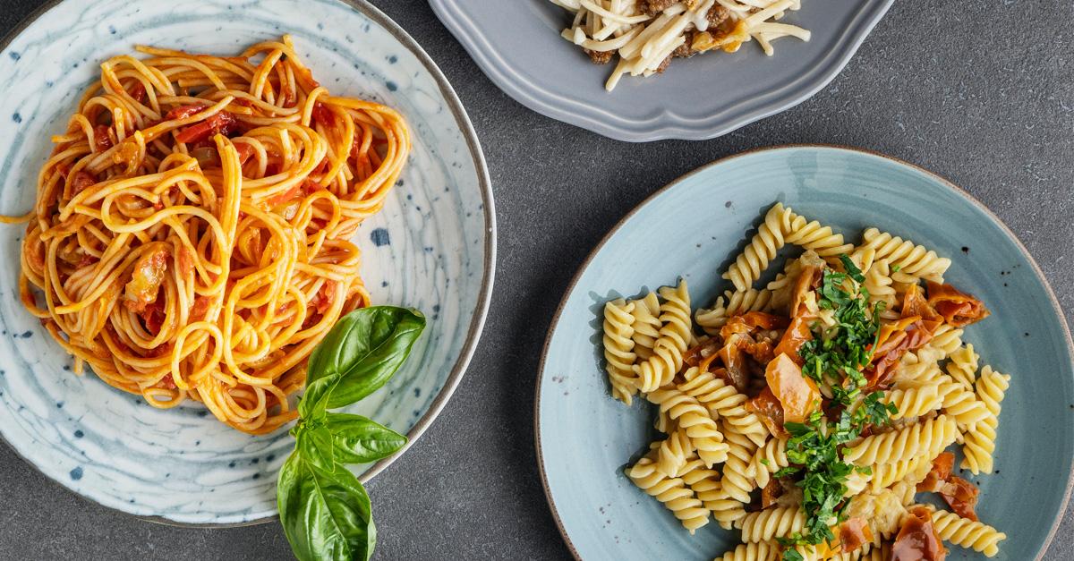 Plates of spaghetti and rotini pasta on a grey surface