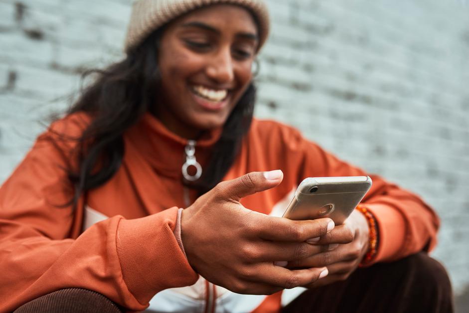 Gen Z girl laughing at her phone while sitting down.