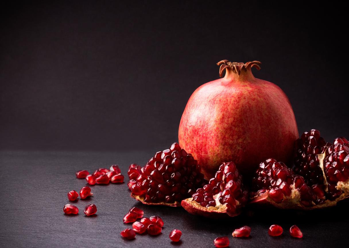 A photo of a pomegranate next to seeds atop a black countertop.