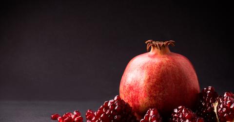 A photo of a pomegranate next to seeds atop a black countertop.