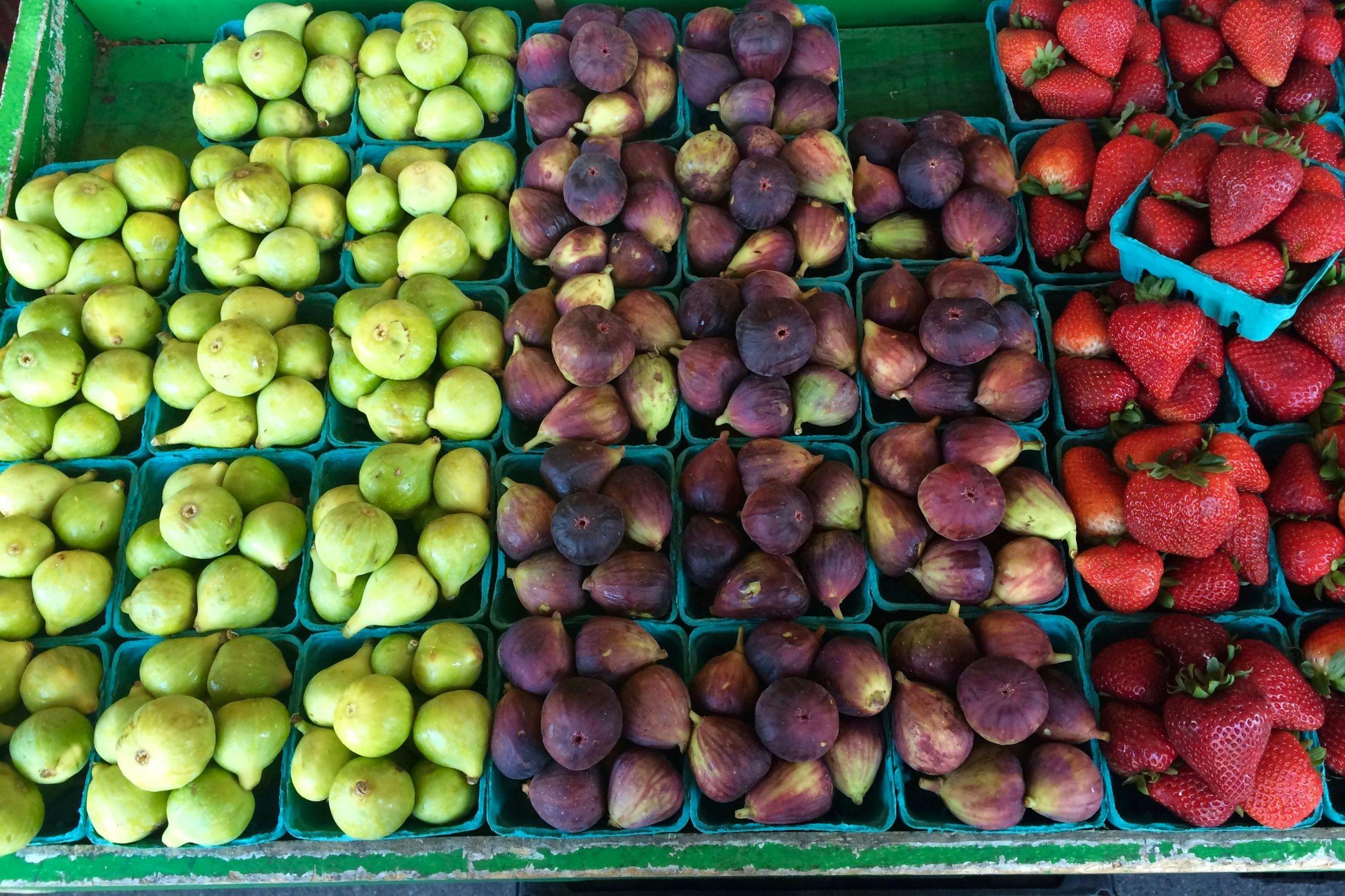 Figs of various colors and sizes are pictured beside strawberries at a farmers market.