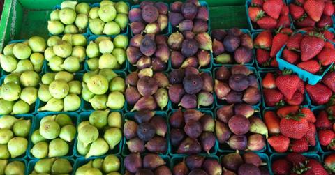 Figs of various colors and sizes are pictured beside strawberries at a farmers market.