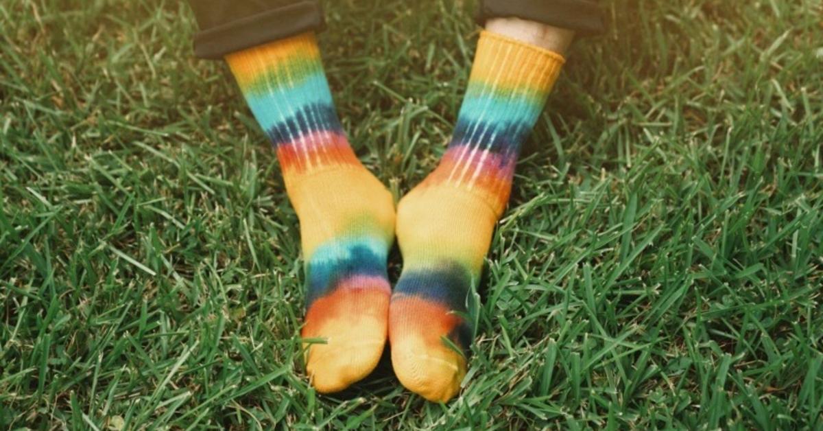 Person's feet wearing tie dye Maggie's Organics socks on grass