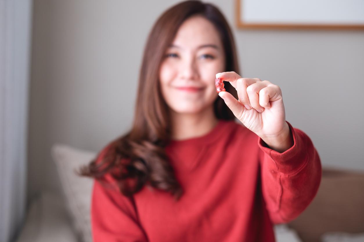 A smiling woman in a red sweater holds a gummy up with her hands in the foreground.