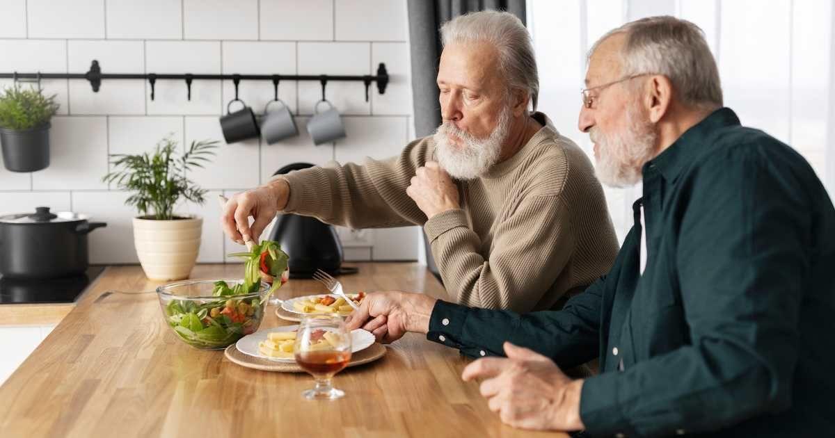 Two elderly men enjoy a hearty meal in the kitchen. (Representative Cover Image Source: FreePik | freepik)