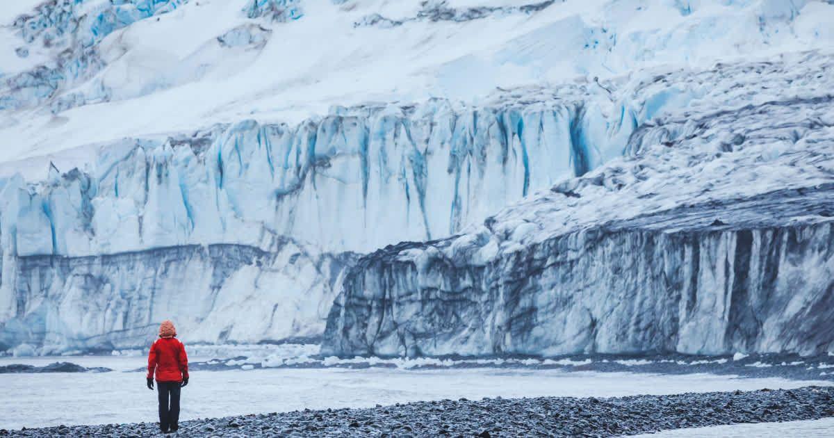 A man standing in front of a massive glacier. (Representative Cover Image Source: Getty Images | anyaberkut)