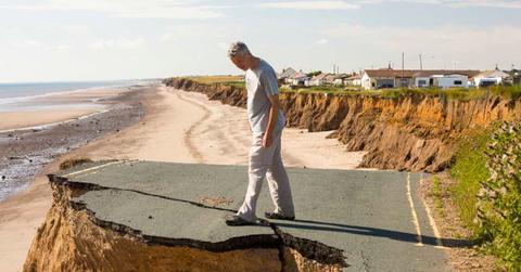 Man standing on a collapsed coastal road near a beach. (Representative Cover Image Source: Getty Images | Ashley Cooper)
