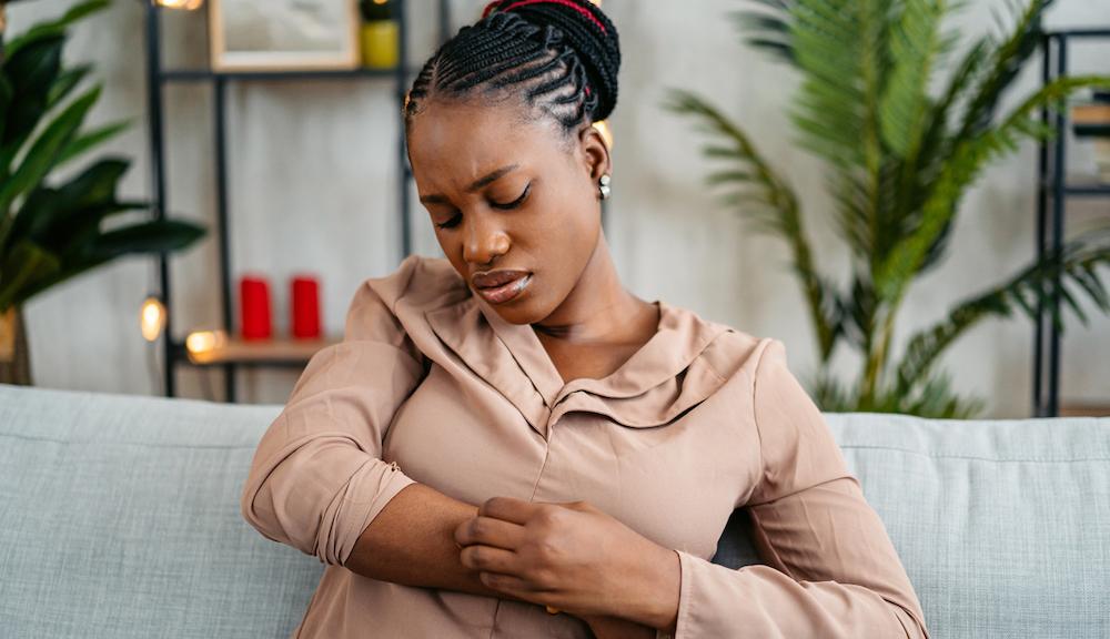 A woman scratching at her arm on the couch.