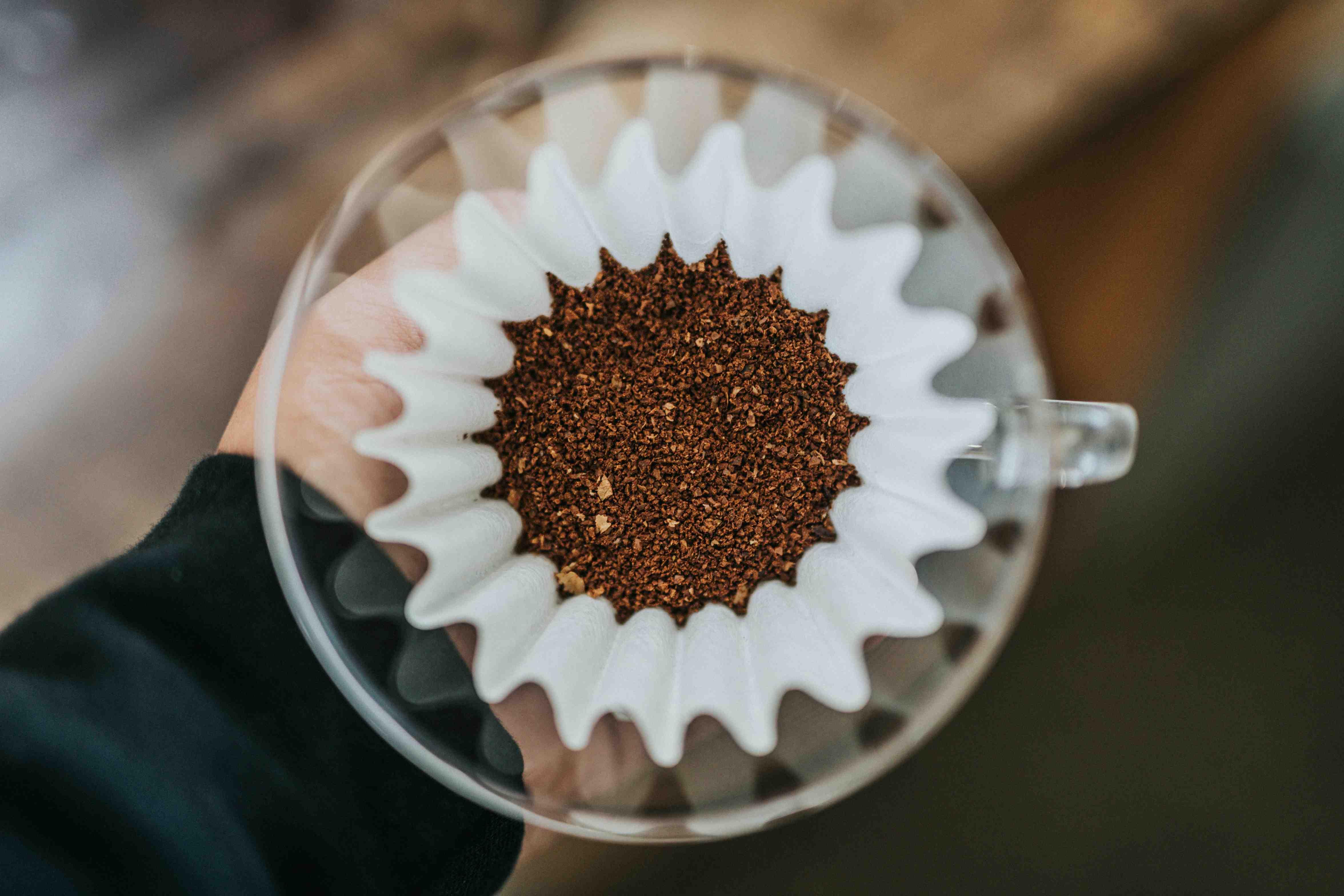 Coffee grounds are pictured in a white filter inside a glass container.