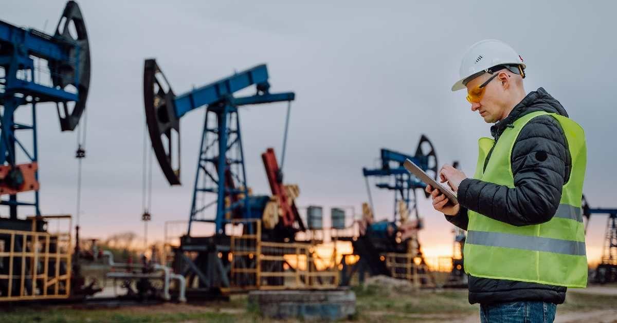 An engineer in protective gear at an oil field with oil pumps in the background. (Representative Cover Image Source: Getty Images | Olga Rolenko)