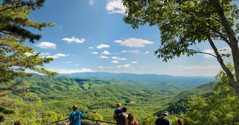 Tourists at a scenic outlook in the Smoky Mountains that overlooks green foliage, mountains, and blue skies.