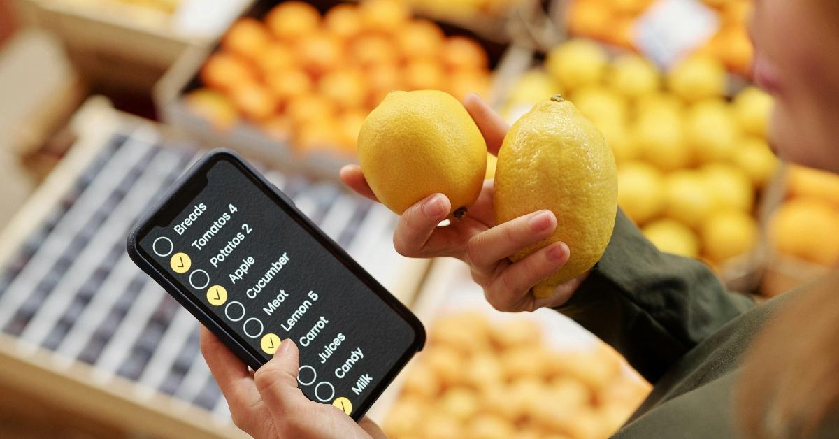 Close-up photograph of a woman using a grocery list in her phone while holding a lemon.