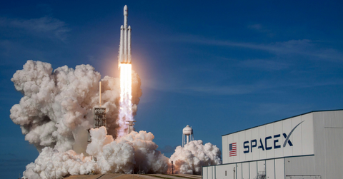 A rocket launches in front of a SpaceX sign